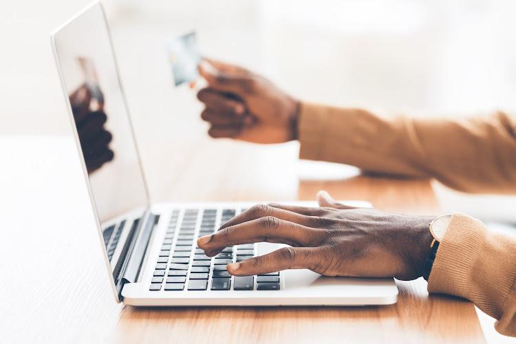 A close-up of a hand typing on a laptop, while the other hand holds a credit card, suggesting online shopping or payment.