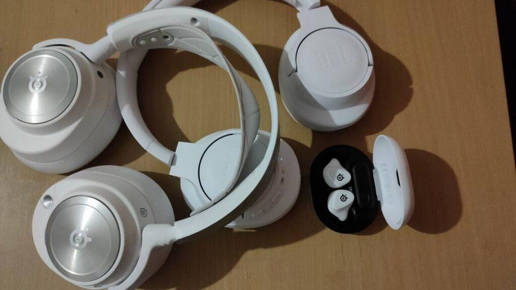 A pair of white over-ear headphones and a set of white wireless earbuds displayed on a wooden surface.