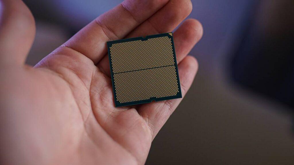 A person holds a computer CPU with a grid of metallic pins, showcasing its intricate design against a blurred background.