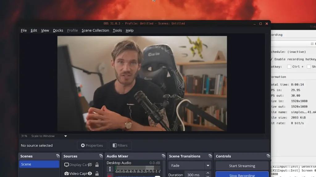 PewDiePie is seated in front of a computer setup with a microphone, surrounded by bookshelves and a plant in the background.