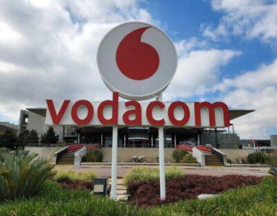 Vodacom headquarters sign with a large logo, surrounded by greenery and cloudy skies in the background.