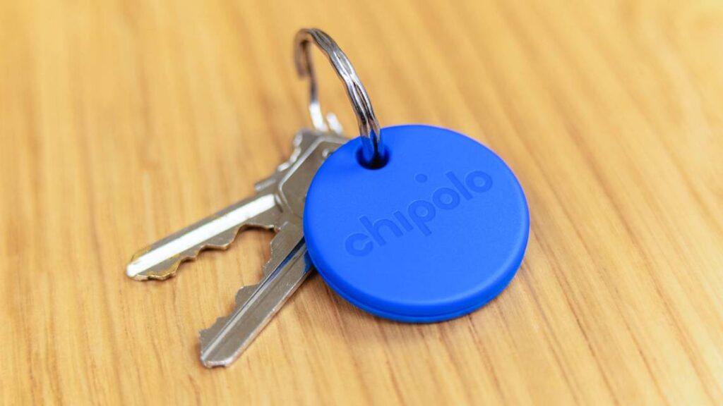 A blue Chipolo key tracker sits next to several keys on a wooden surface.