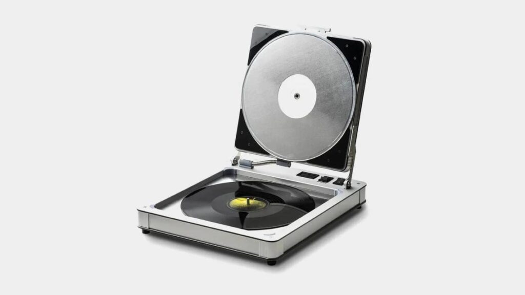A silver, open turntable displaying a black vinyl record on its platter, set against a minimalist white background.
