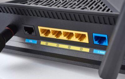 Close-up of a black router's back panel showing DSL and E-WAN ports, four yellow LAN ports, and connection indicators.