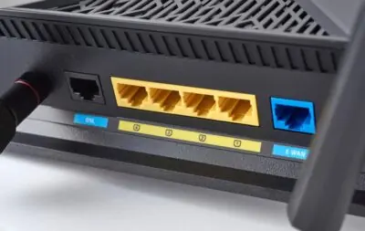 Close-up of a black router's back panel showing DSL and E-WAN ports, four yellow LAN ports, and connection indicators.