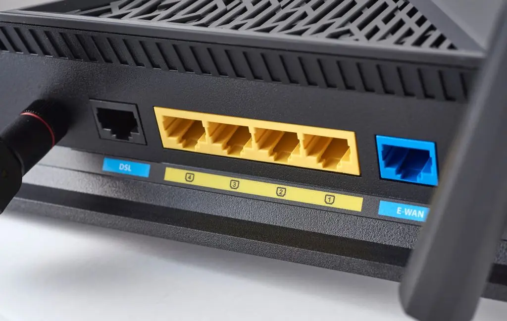 Close-up of a black router's back panel showing DSL and E-WAN ports, four yellow LAN ports, and connection indicators.