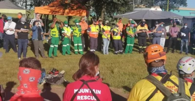 Ham radio turns 100 in South Africa 10 A diverse group of rescue volunteers in uniforms, gathered outdoors for a briefing, with tents in the background and masks on.