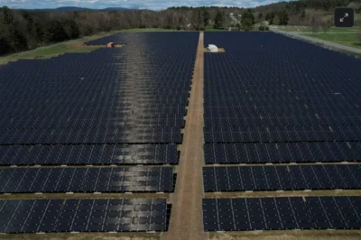 Rogue communication devices found in Chinese solar power inverters 2 Aerial view of a vast solar farm featuring rows of black solar panels under a clear sky, with green fields and trees in the background.