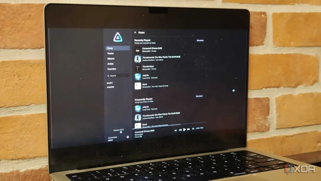 A laptop screen displaying a music app with recently and frequently played tracks, on a brick wall background.