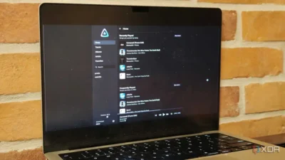 A laptop screen displaying a music app with recently and frequently played tracks, on a brick wall background.