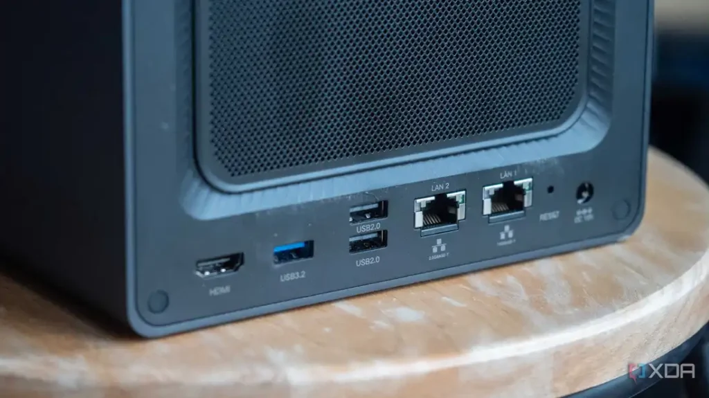 Close-up of a computer case's rear panel showing HDMI, USB ports, LAN connectors, and a reset button. Decorative wooden surface below.