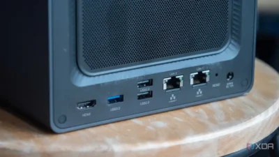 Close-up of a computer case's rear panel showing HDMI, USB ports, LAN connectors, and a reset button. Decorative wooden surface below.