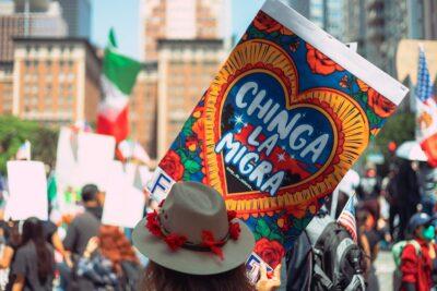 Using Signal groups for activism 7 A person holds a colorful sign reading "CHINGA LA MIGRA," surrounded by a crowd at a vibrant street protest celebrating immigrant rights.