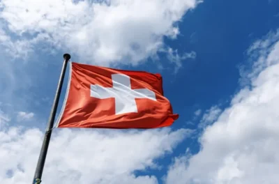 Switzerland releases its own AI model trained on public data and its open source 9 Switzerland's red flag with a white cross fluttering against a bright blue sky with fluffy clouds.