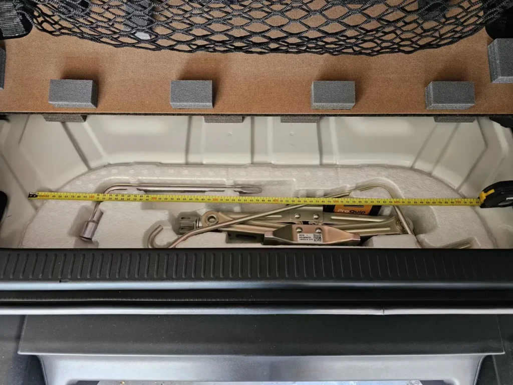 Image of a truck bed storage compartment with a Pro Quip jack, measuring tape, and tool components neatly arranged on foam padding.