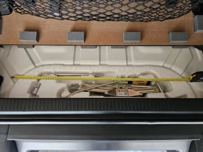 Image of a truck bed storage compartment with a Pro Quip jack, measuring tape, and tool components neatly arranged on foam padding.
