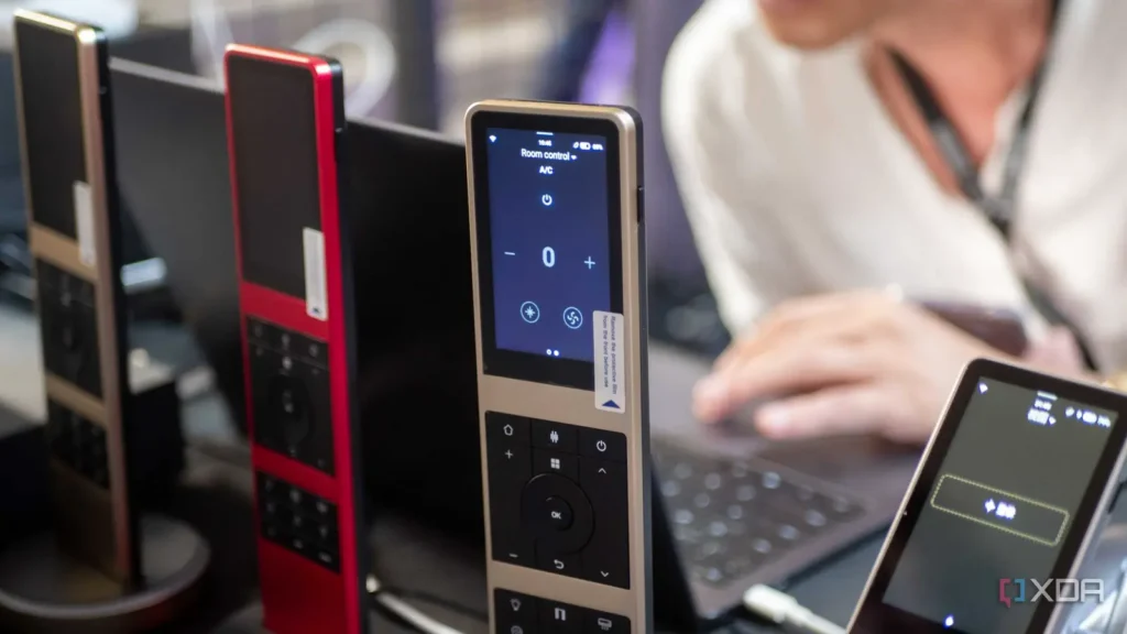 A close-up of sleek room control devices in gold and red, with a user interacting with a laptop in the blurred background.