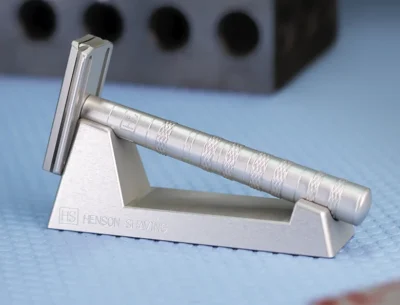 A sleek silver safety razor rests on a stand, showcasing its modern design and textured grip.
