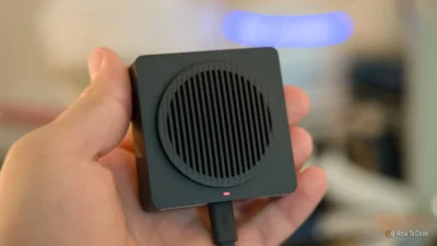 These video doorbells don’t rely on the cloud or subscriptions 3 A person holding a compact black speaker with a circular speaker grille and a red indicator light, set against a blurred background.