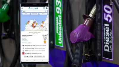Smartphone displaying fuel price and station app next to a purple diesel fuel nozzle at a gas pump.