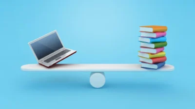Laptop and stack of colorful books balanced on a white seesaw against a blue background.