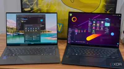Two laptops side by side on a wooden table, one running Windows 11 and the other running a Linux desktop environment.