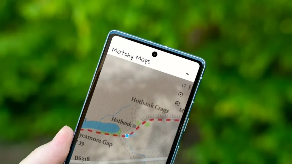 Hand holding a smartphone displaying a map app called "Matchy Maps" with location near Hotbank Crags and Sycamore Gap.