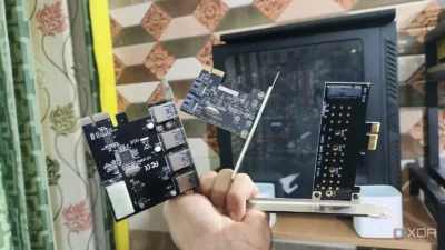 Hand holding three PCIe expansion cards against a background of a desktop PC and patterned wall tiles.