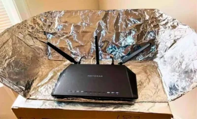 Wi-Fi router with three antennas positioned in a homemade reflector made of aluminum foil to boost signal strength.