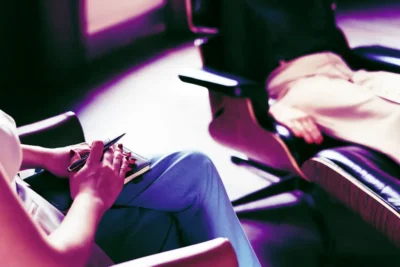 Two people seated facing each other, one holding a pen and notebook, suggesting a counseling or therapy session.