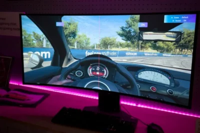 LG Monitors Fill Windows PCs With Adware, and It’s Not Just Recent Displays 4 Curved monitor displaying a first-person car racing game, with a steering wheel and dashboard visible, set against a pink LED-lit desk.