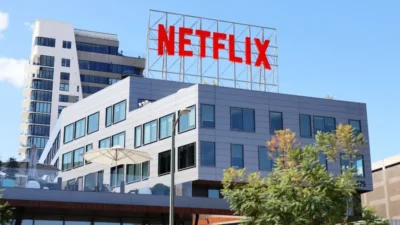 Modern office building with large red "NETFLIX" sign on the rooftop under a clear blue sky.