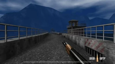 First-person view of a video game character holding a rifle on a concrete bridge with guard towers and mountains in the background at night.